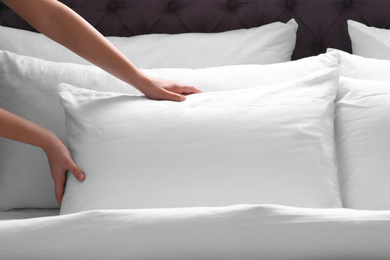 Photo of Woman fluffing white pillow on bed, closeup