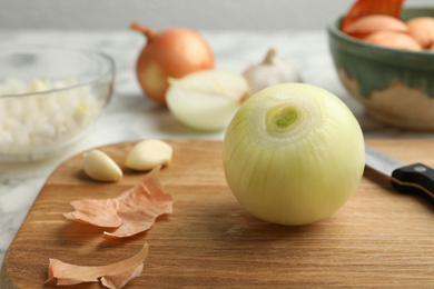Photo of Peeled onion and knife on wooden board, closeup