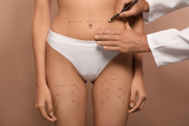 Doctor with pencil preparing patient for cosmetic surgery operation on light brown background, closeup