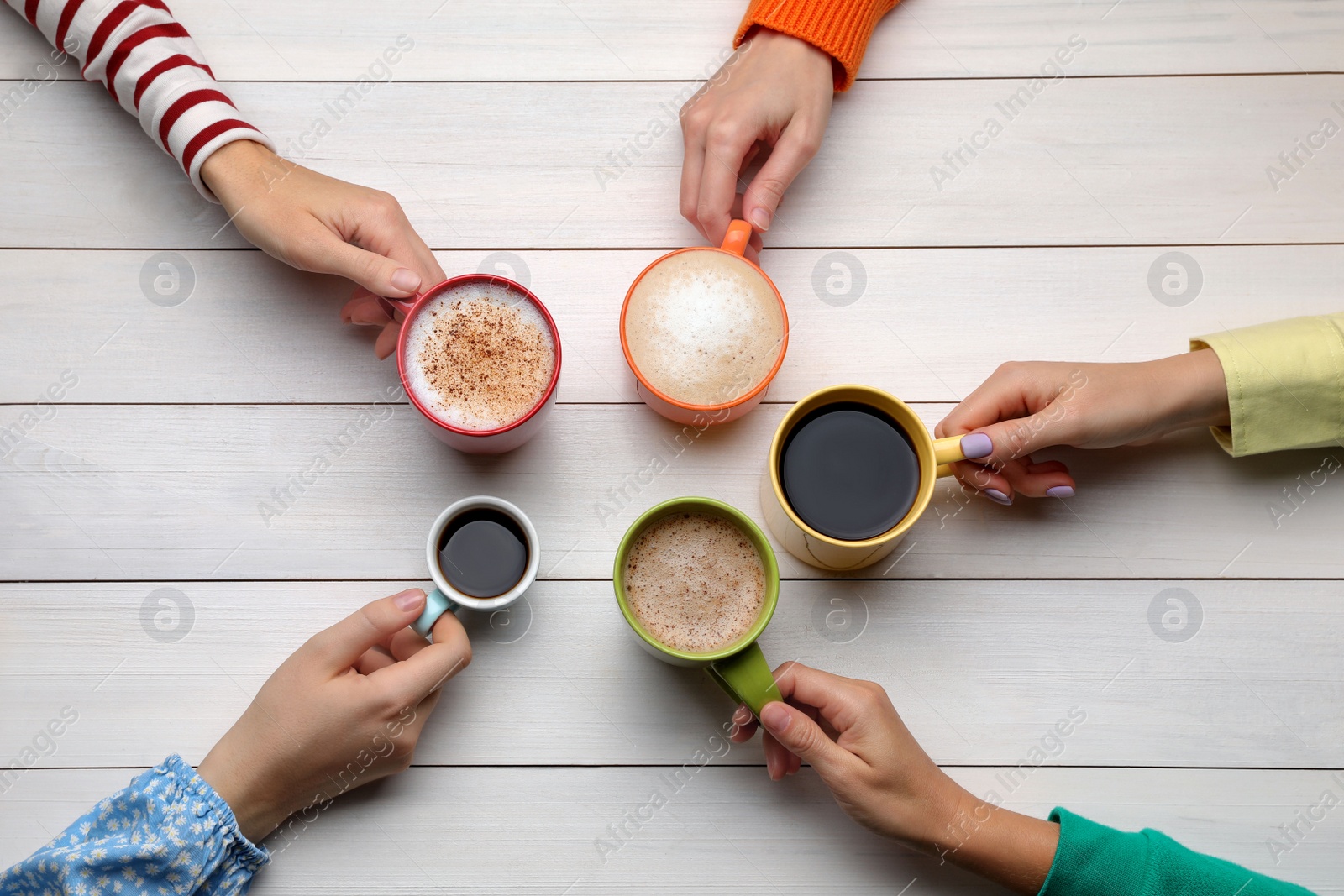 Photo of People holding different cups with aromatic hot coffee at white wooden table, top view
