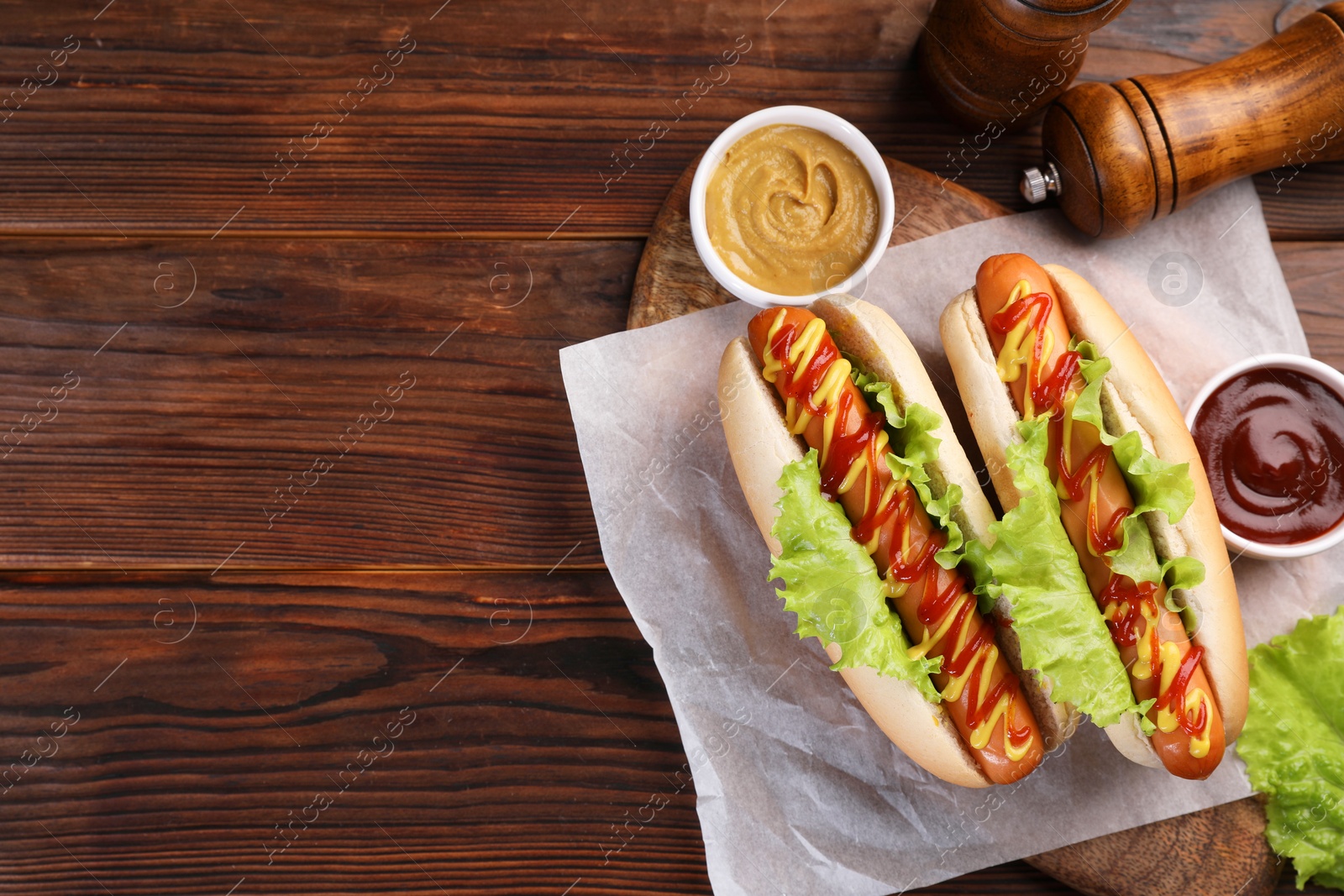 Photo of Tasty hot dogs with lettuce, ketchup and mustard on wooden table, top view. Space for text