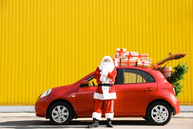 Photo of Authentic Santa Claus near red car with gift boxes and Christmas tree, outdoors