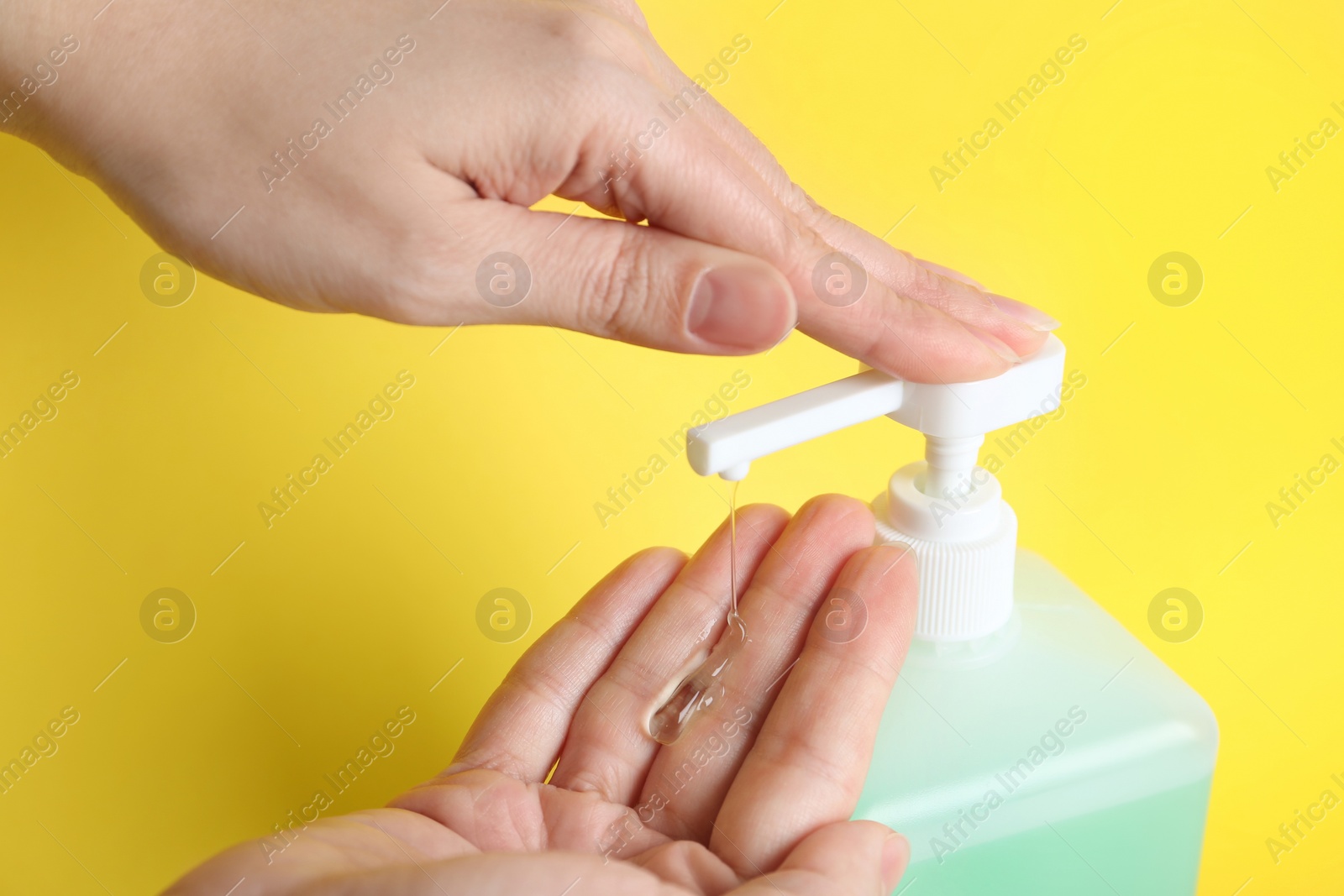 Photo of Woman applying antiseptic gel on hand against yellow background, closeup