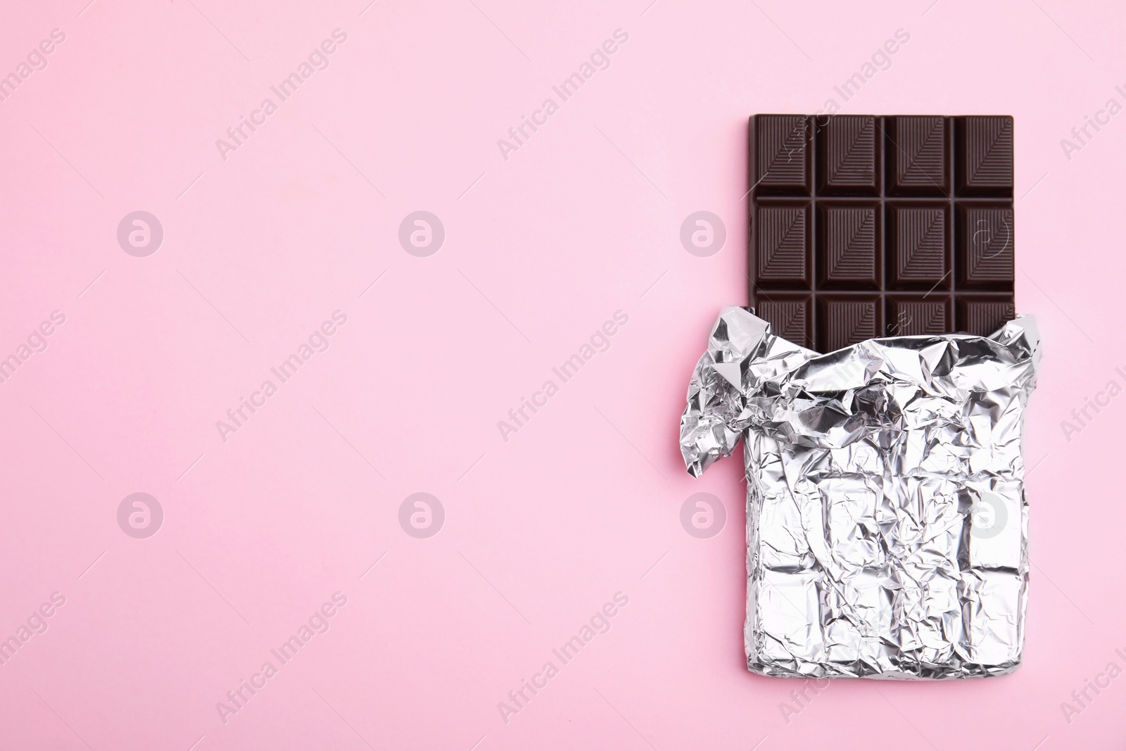 Photo of Tasty chocolate bar on pink background, top view. Space for text