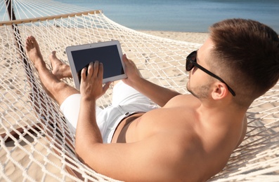 Photo of Young man with tablet in hammock on beach