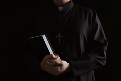 Photo of Priest with Bible on dark background, closeup