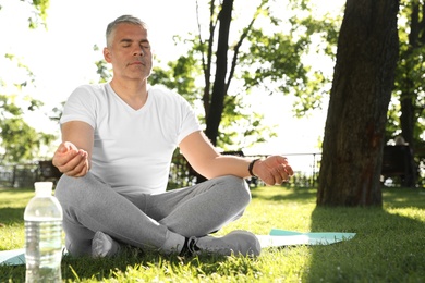 Photo of Handsome mature man practicing yoga in park, space for text. Healthy lifestyle