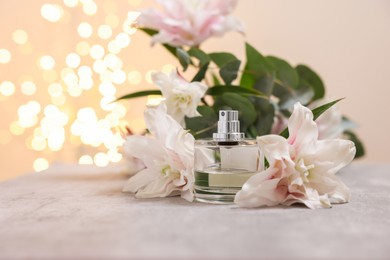 Photo of Bottle of perfume and beautiful lily flowers on table against beige background with blurred lights, closeup