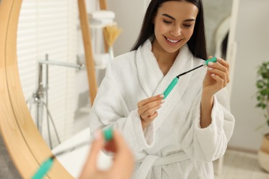 Photo of Beautiful young woman with mascara in bathroom