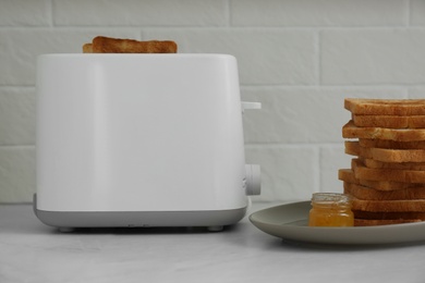 Photo of Modern toaster with slices of bread and honey on white table in kitchen
