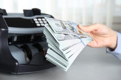 Woman holding money near counting machine at table indoors, closeup