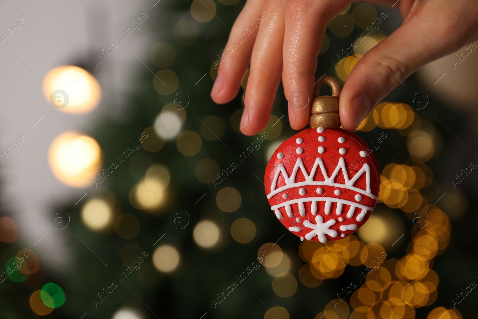 Photo of Woman holding Christmas macaron against blurred festive lights, closeup. Space for text