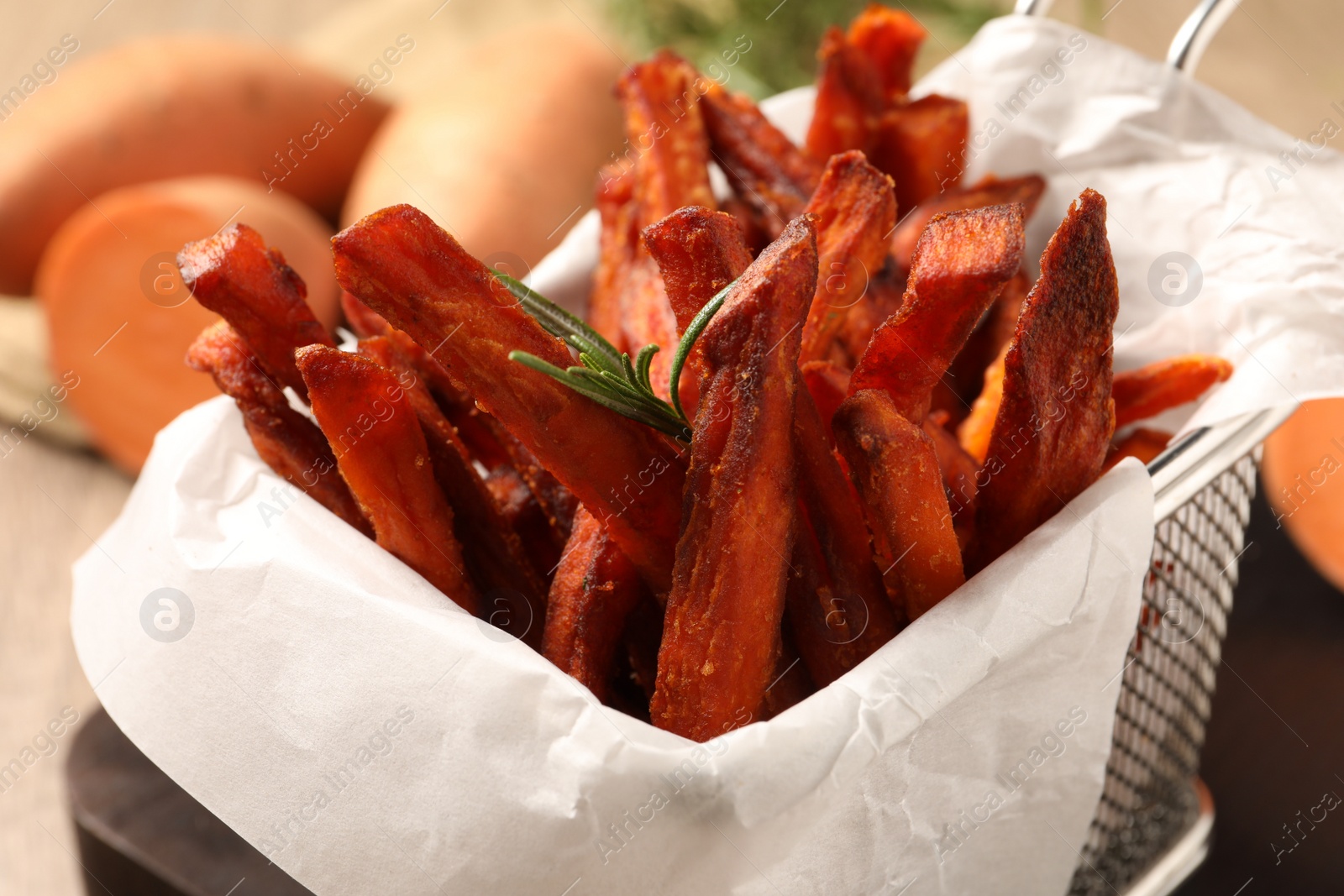 Photo of Frying basket with sweet potato fries on table, closeup