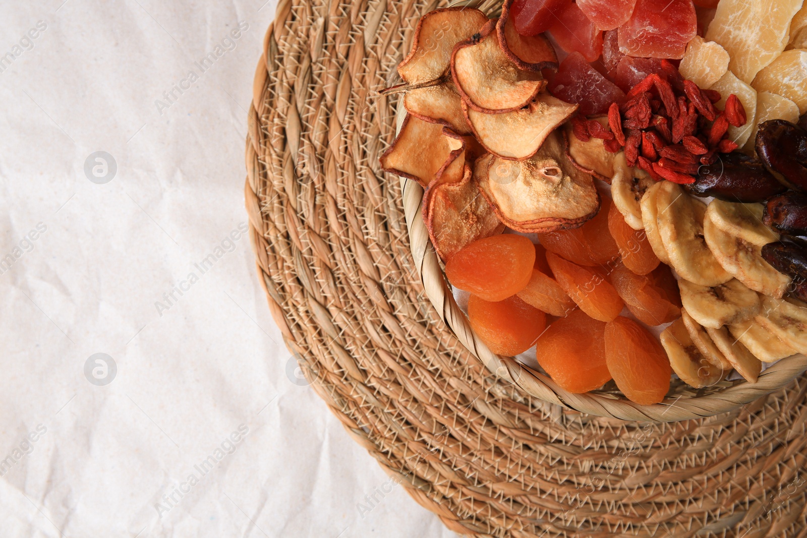 Photo of Wicker basket with different dried fruit on paper, top view. Space for text