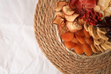 Photo of Wicker basket with different dried fruit on paper, top view. Space for text