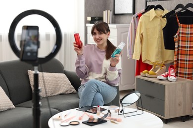 Smiling beauty blogger recording video while showing cosmetic products at home