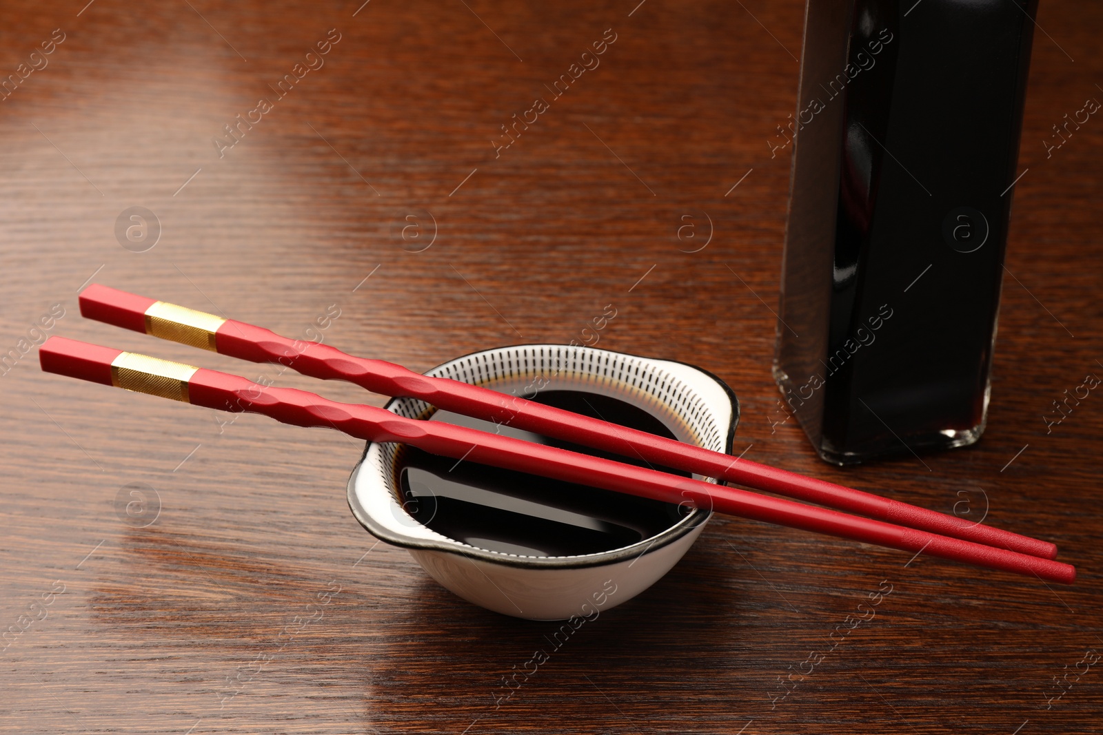 Photo of Bowl, bottle with soy sauce and chopsticks on wooden table