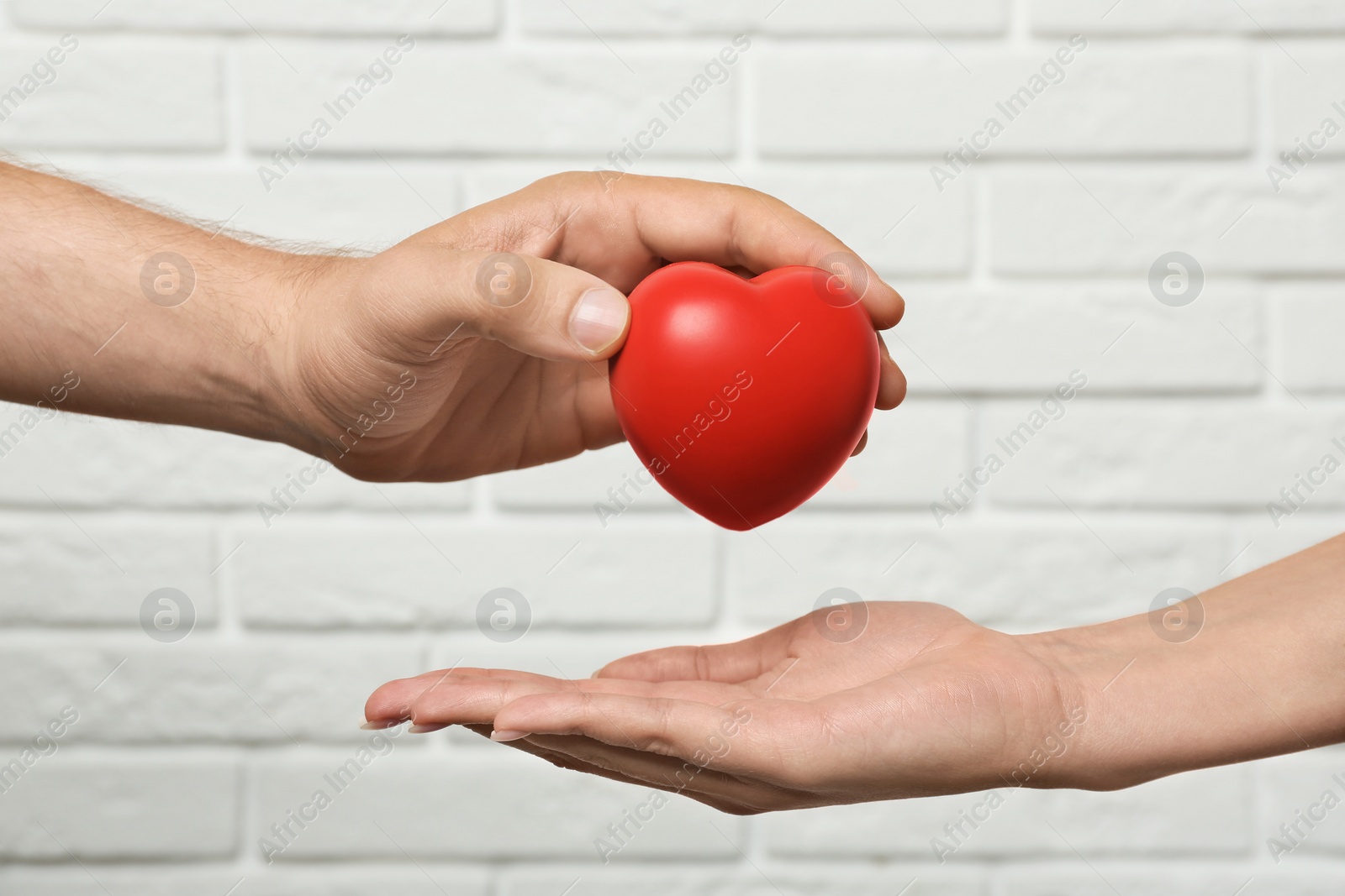 Photo of Man giving red heart to woman at white brick wall, closeup. Donation concept