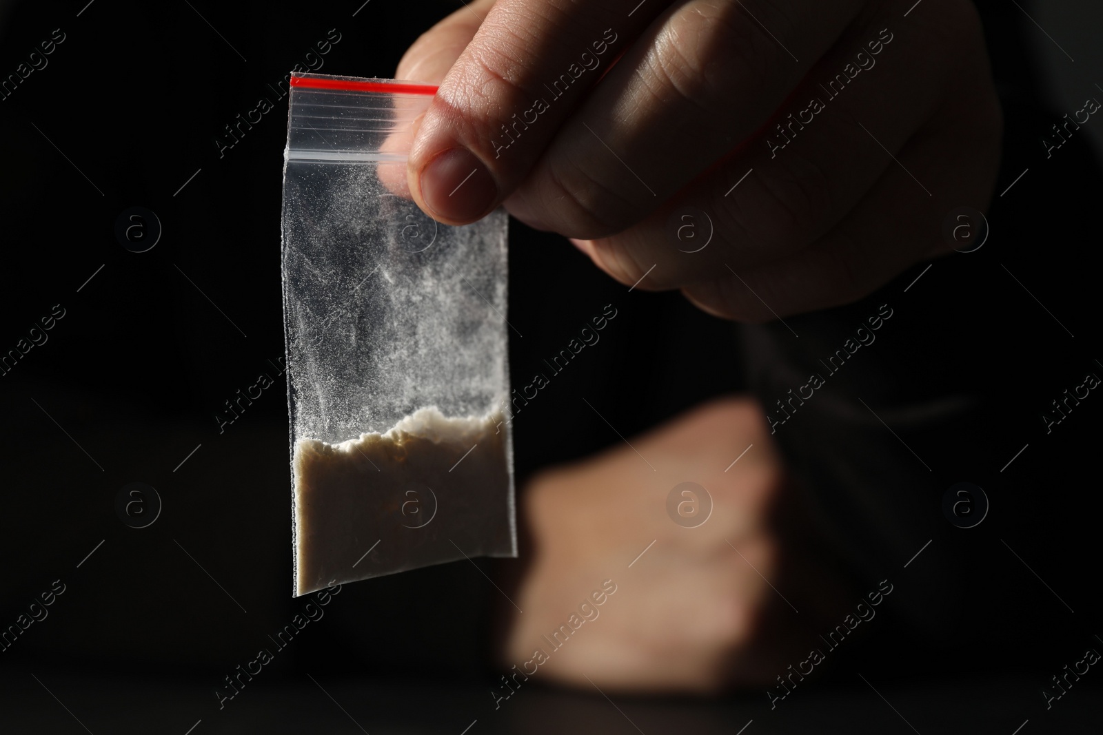 Photo of Drug addiction. Man with plastic bag of cocaine on dark background, closeup