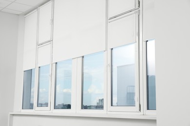 Photo of Plastic windows with white roller blinds indoors