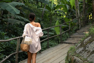 Young woman walking in green tropical park, back view. Space for text