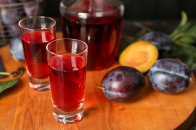 Photo of Delicious plum liquor and ripe fruits on wooden board. Homemade strong alcoholic beverage