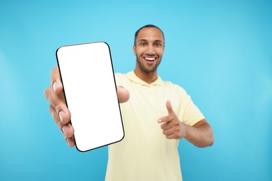 Photo of Young man showing smartphone in hand and pointing at it on light blue background, selective focus. Mockup for design
