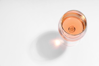 Photo of Rose wine in glass and shadow on white background, top view. Space for text