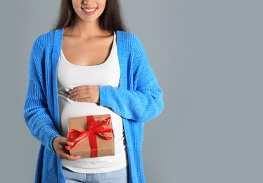 Photo of Happy pregnant woman with Christmas gift box on grey background, closeup. Expecting baby