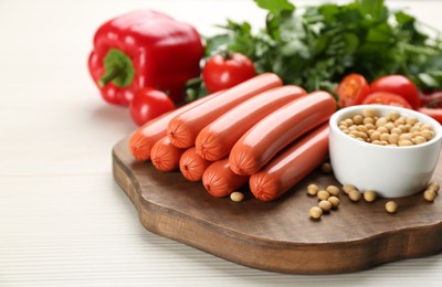 Photo of Fresh raw vegetarian sausages, soybeans and vegetables on white wooden table