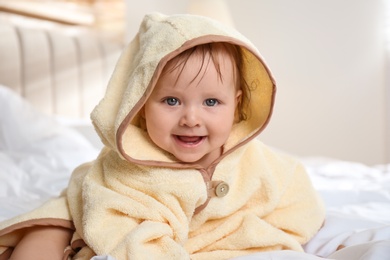 Cute little baby in yellow hooded towel on bed after bath