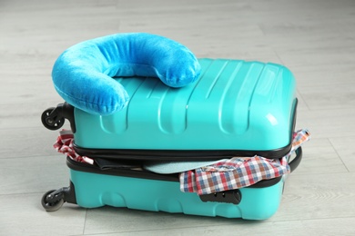 Photo of Suitcase with clothes and travel pillow on wooden floor