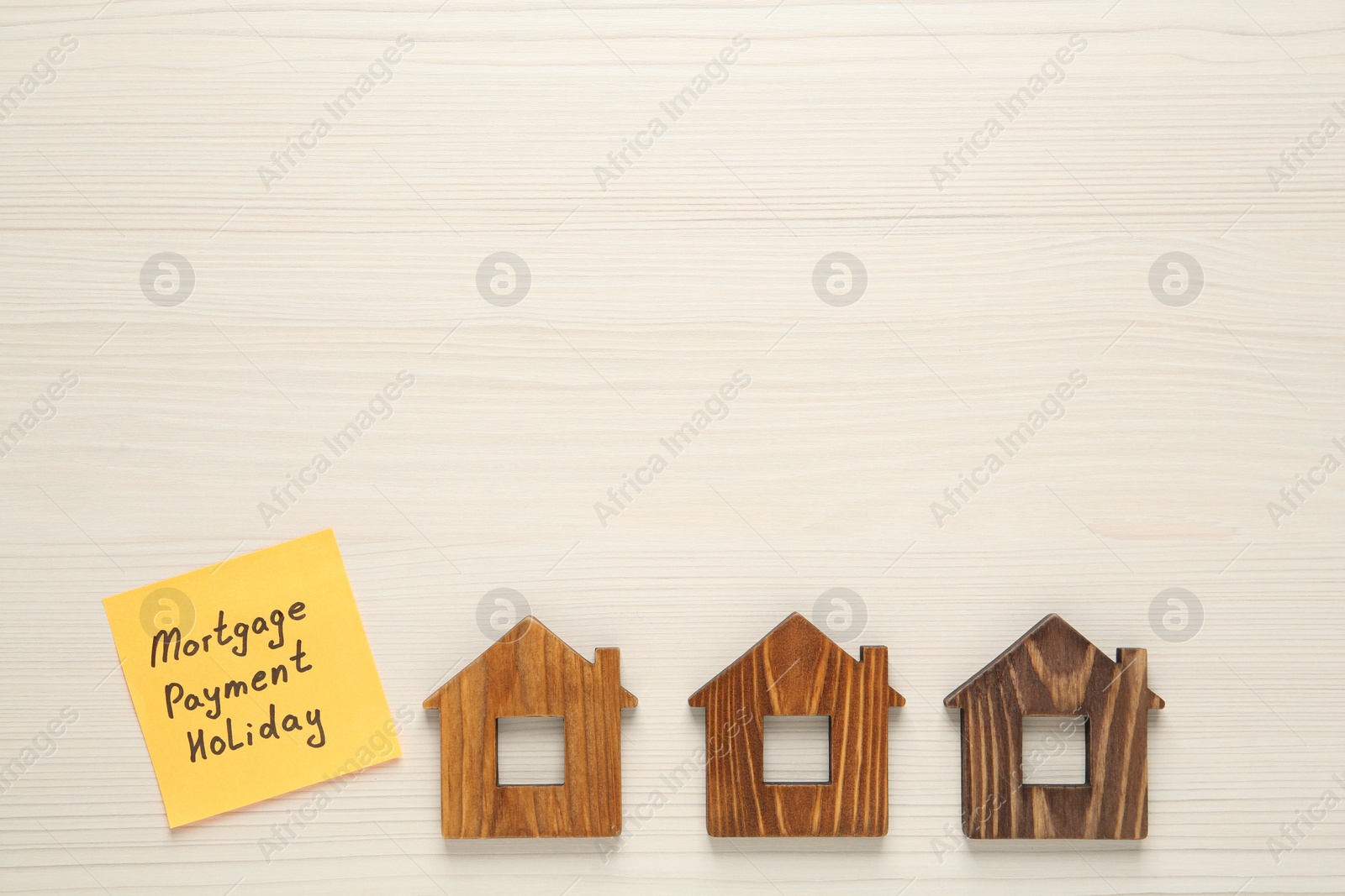 Photo of Paper note with words Mortgage Payment Holiday and house models on white wooden table, flat lay. space for text