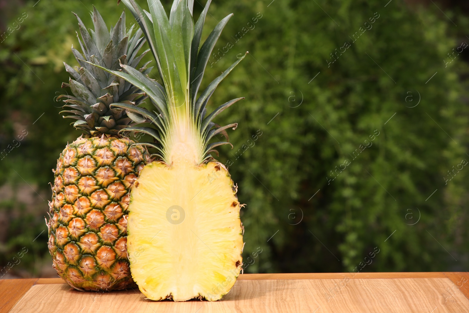 Photo of Delicious ripe pineapples on wooden table outdoors, space for text