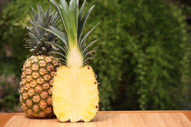 Photo of Delicious ripe pineapples on wooden table outdoors, space for text