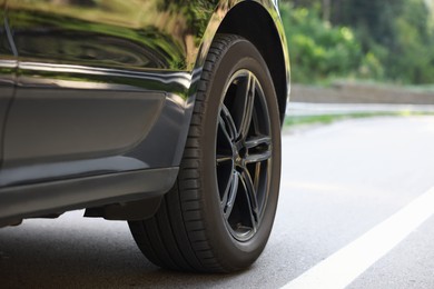 Modern black car on asphalt road outdoors, closeup. Space for text