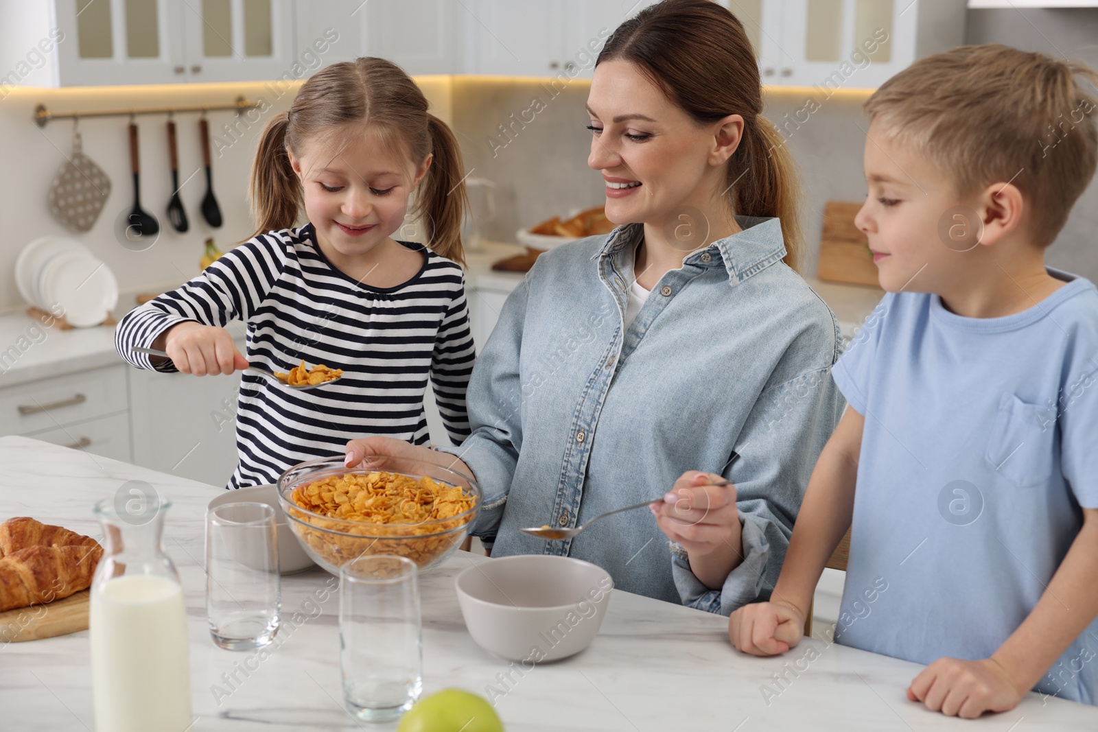 Photo of Mother and her little children having breakfast at table in kitchen