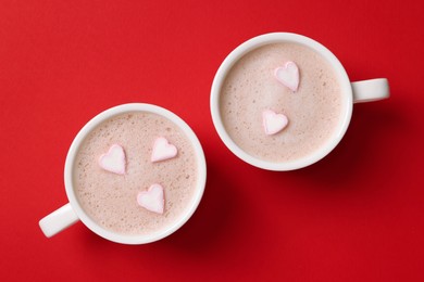 Cups of aromatic coffee with heart shaped marshmallows on red background, flat lay