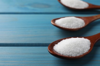 Photo of Granulated sugar in spoons on turquoise wooden table, closeup. Space for text