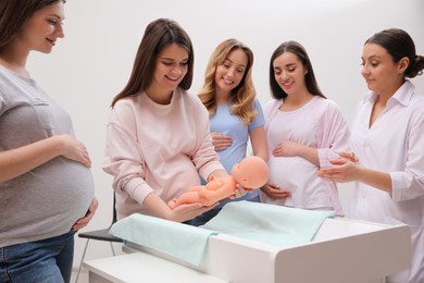 Photo of Pregnant women learning how to swaddle baby at courses for expectant mothers indoors