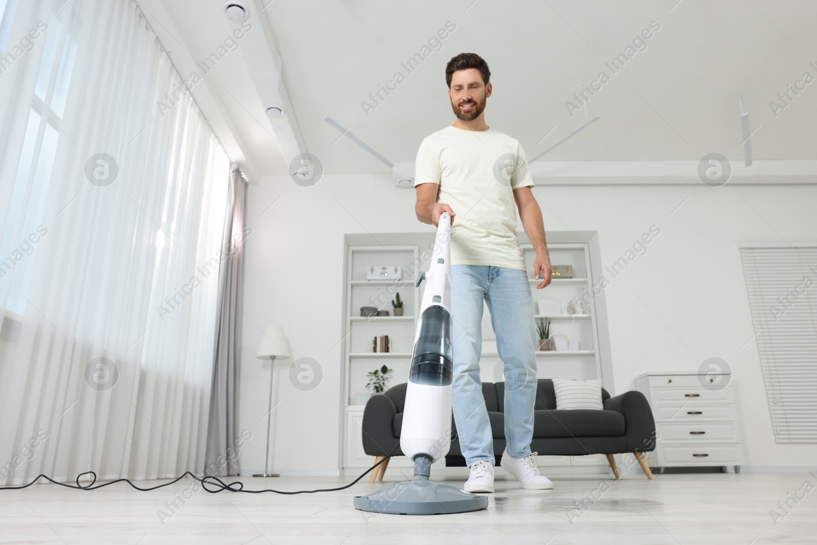 Photo of Happy man cleaning floor with steam mop at home, low angle view