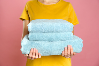 Woman holding stack of fresh towels on pink background, closeup