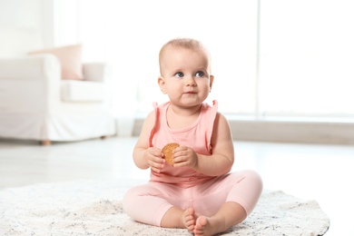 Photo of Cute baby girl with cookie on floor in room