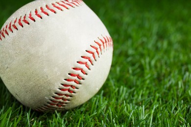 Worn baseball ball on green grass, closeup. Space for text