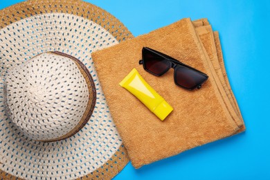 Photo of Straw hat, sunscreen, sunglasses and towel on light blue background, flat lay
