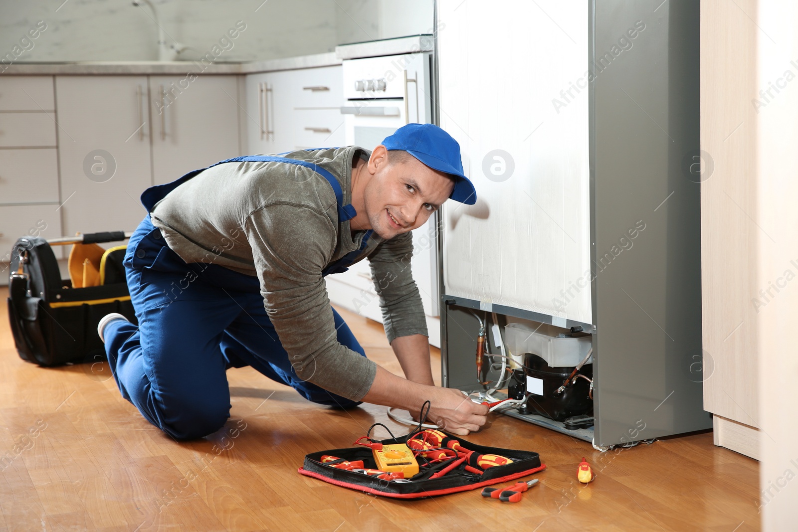 Photo of Male technician in uniform repairing refrigerator indoors