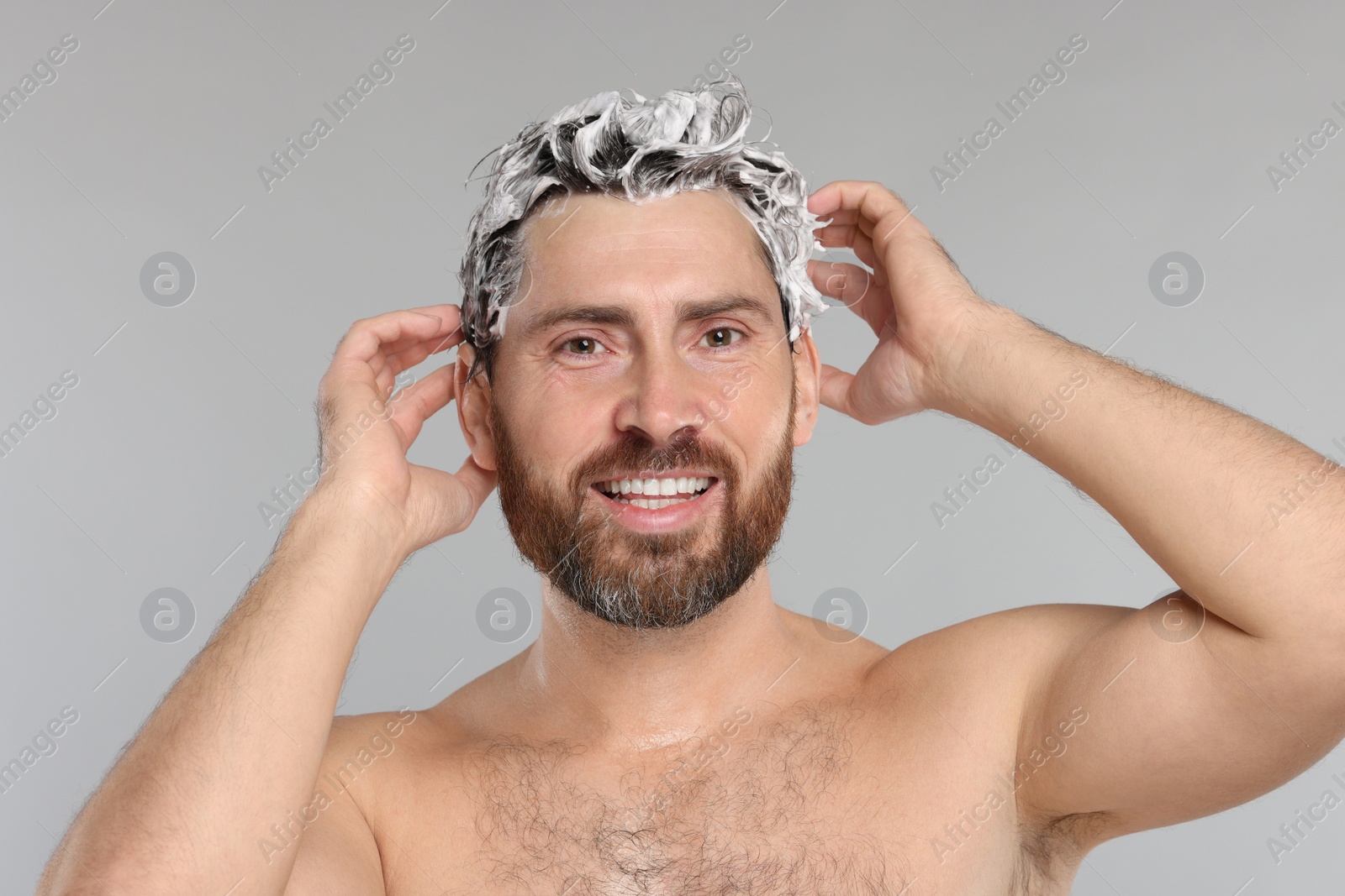 Photo of Happy man washing his hair with shampoo on grey background