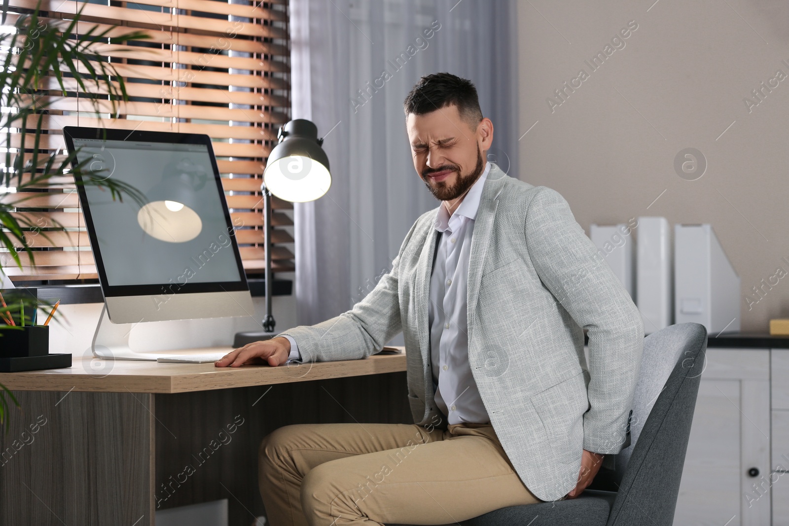 Photo of Man suffering from hemorrhoid at workplace in office