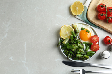 Photo of Oven baked asparagus served with fried egg on light grey marble table, flat lay. Space for text