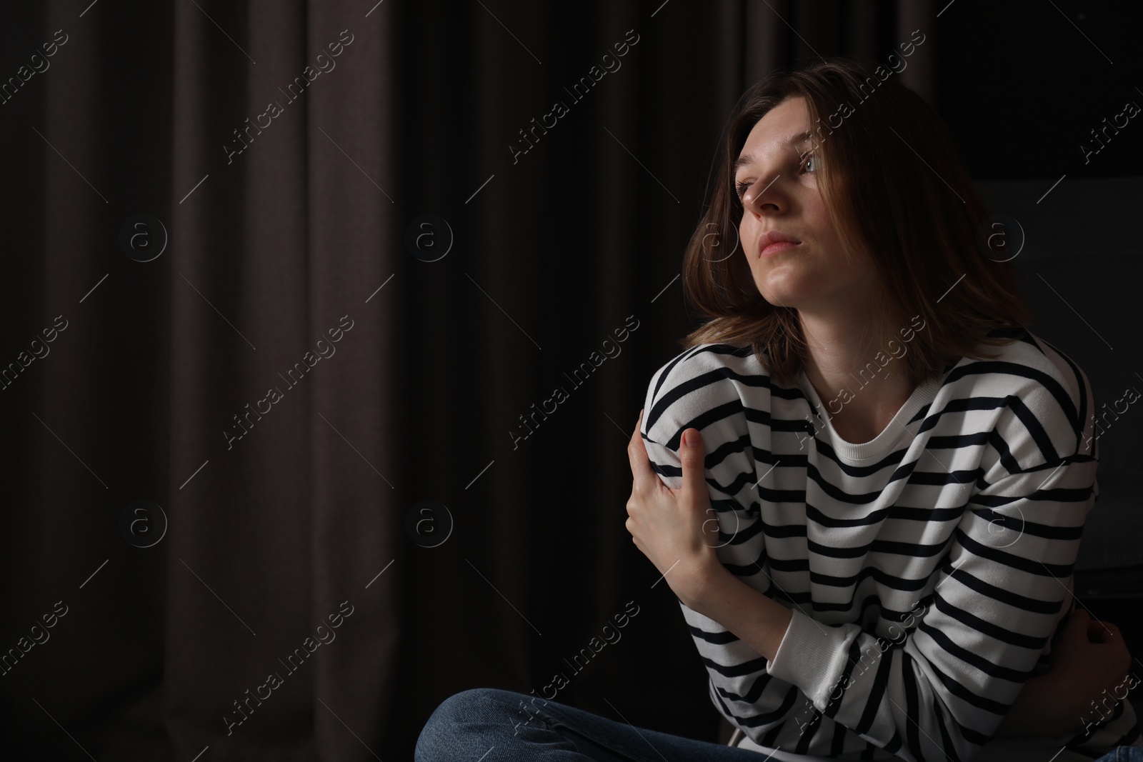 Photo of Sad young woman near curtains indoors, space for text